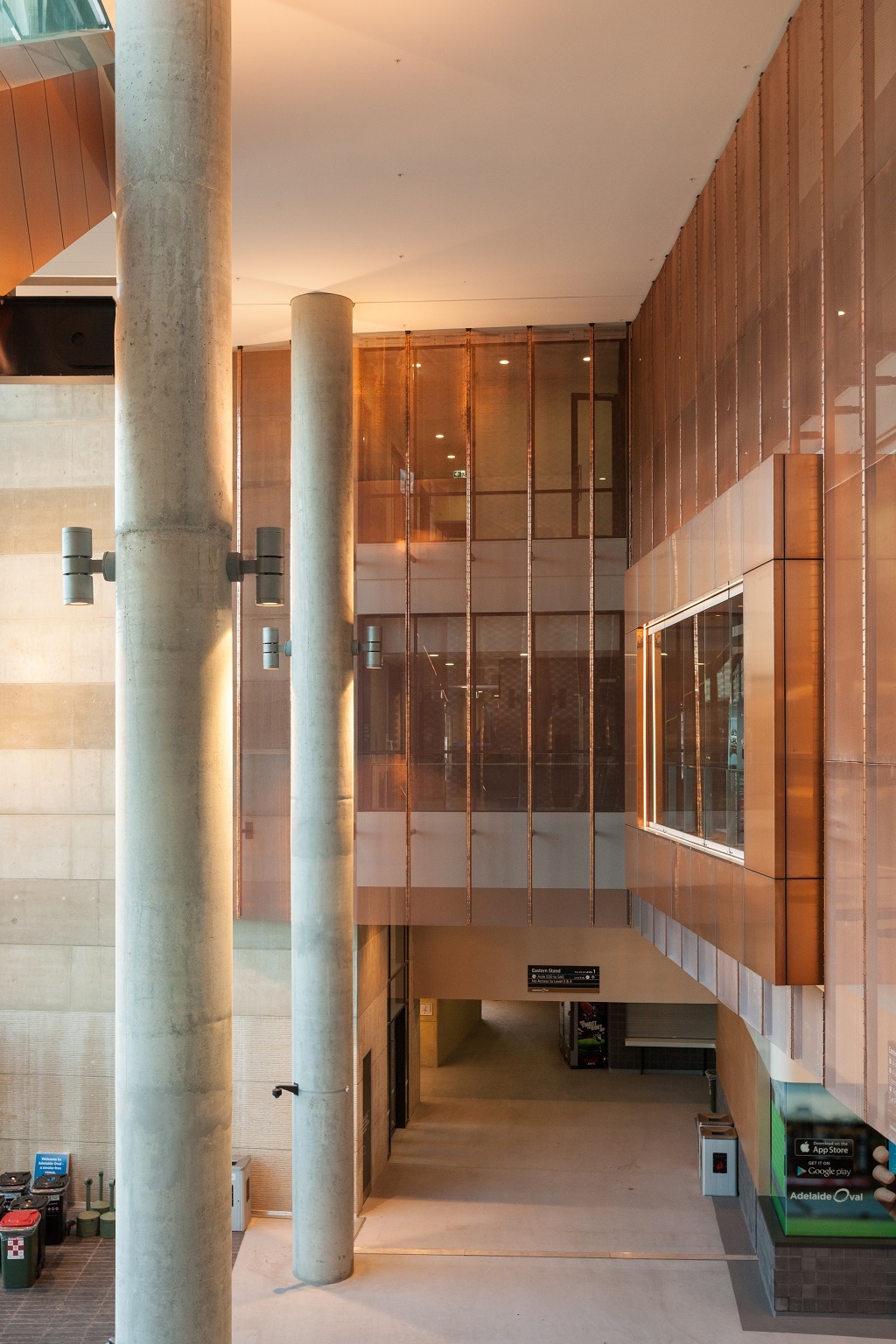 Interior of the Adelaide Oval building. Walls are decorated with Nordic Bronze clad volumes and mesh. Concrete Pillars rise from the ground level to the ceiling.