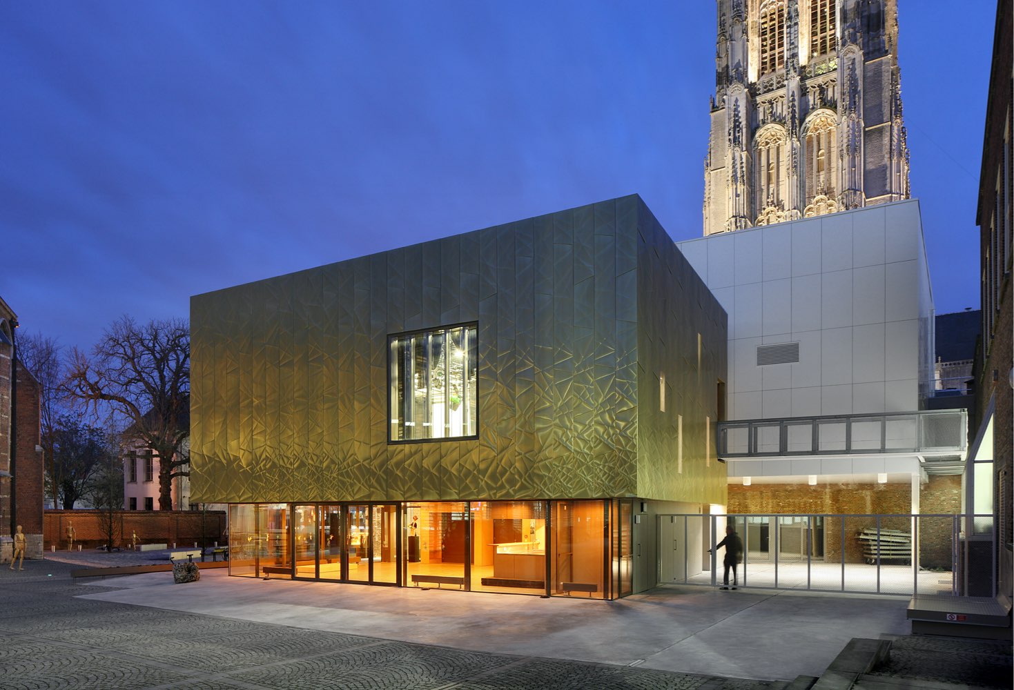Side panel of Mechelen Moon Art Centre located in Mechelen, Belgium. The panel is made from Nordic Royal Copper and it is gold-coloured. The copper has small folds and creases. The wall is seen from very close. There is a light source in the panel.