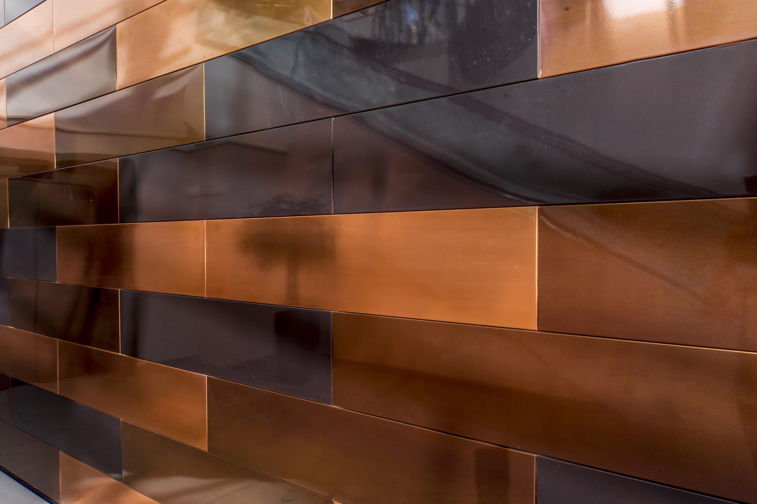 Copper panel covered wall inside the Onslow Building. Panels are alternating with three different surfaces of Nordic Standard and two different shades of Nordic Brown. Other side of the room can be seen slightly reflecting from the panels.